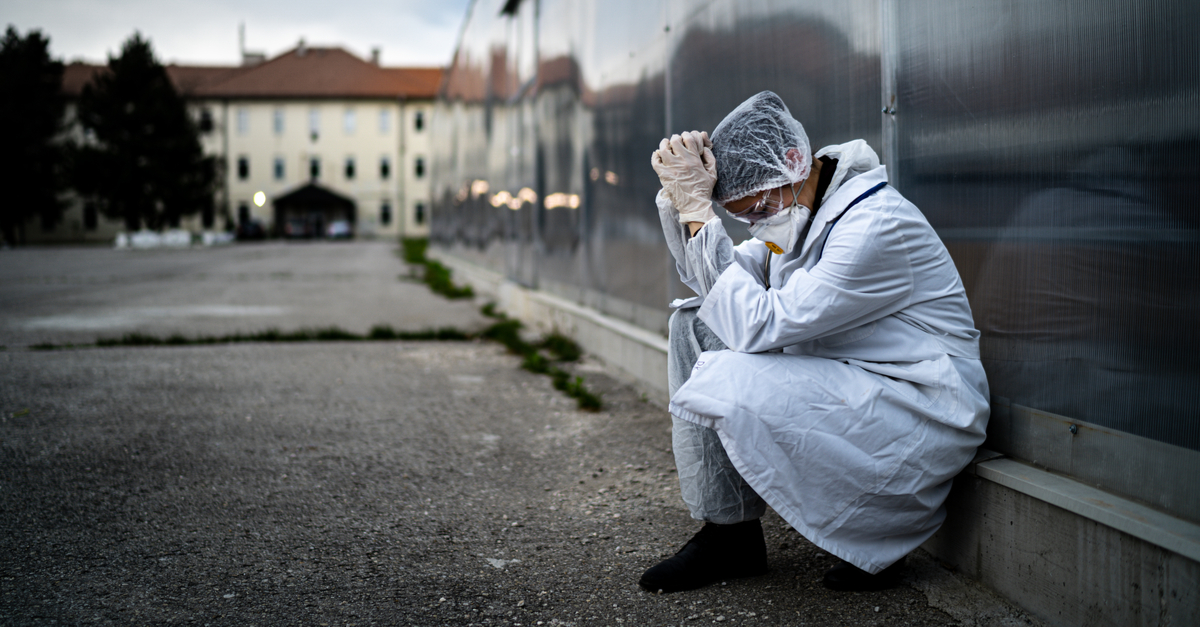 health care worker with mask and hazmat gear crouching and leaning on wall in distress